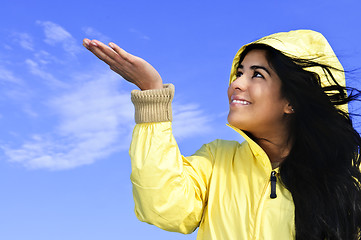 Image showing Beautiful young woman in raincoat checking for rain