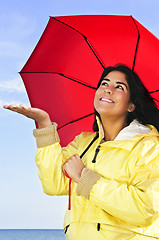 Image showing Beautiful young woman in raincoat with umbrella checking for rain