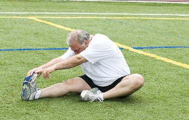 Image showing middle age man stretching and exercising on sports field