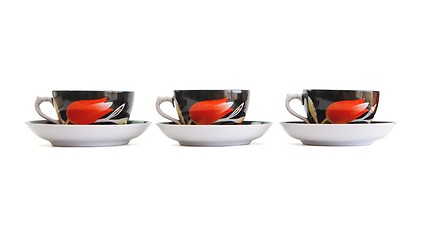 Image showing Row of three black tea cups with saucers isolated 
