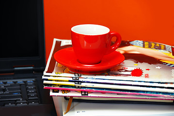Image showing Red cup on magazines and notebook over red