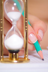 Image showing Female hand with a pencil and a sand clock