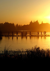 Image showing A group of people walking on the footpath on the lake at sunset