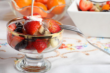 Image showing Cream being poured on Fresh fruit salad in a glass bowl