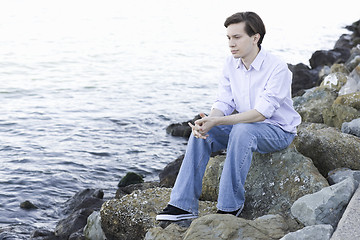 Image showing Teenage Boy Sitting On Rocks By Ocean