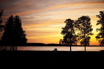 Image showing Elderly couple sitting on a bench by lake at sunset