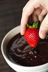 Image showing Hand dipping strawberry in chocolate