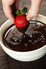 Image showing Hand dipping strawberry in chocolate