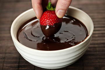 Image showing Hand dipping strawberry in chocolate