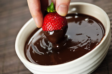 Image showing Hand dipping strawberry in chocolate