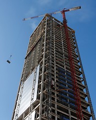 Image showing Lifting crane hoisting a weight at skyscraper construction site
