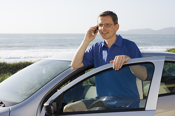 Image showing Man talking on cell phone beside a car at the sea