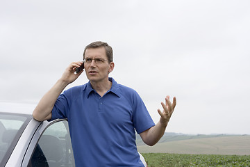 Image showing Angry man talking on cell phone beside a car