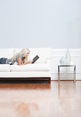 Image showing Young Woman Lying on Sofa Reading Book