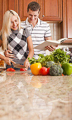 Image showing Young Man Holding Book Next to Woman Cutting Tomato