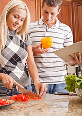 Image showing Young Man Holding Book Next to Woman Cutting Tomato