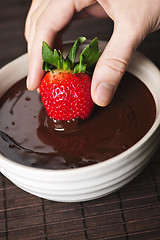 Image showing Hand dipping strawberry in chocolate