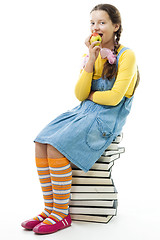 Image showing  girl sit on pile of books and eat apple