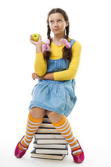 Image showing Girl eat apple sitting on pile of books