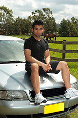 Image showing Man sitting on bonnet of silver car in countryside