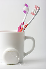 Image showing Two toothbrushes in a cup and dental floss