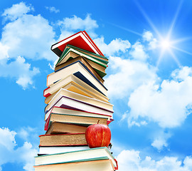 Image showing Pile of books and apple against blue sky