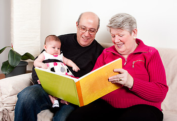 Image showing Grandparents reading book to baby girl.