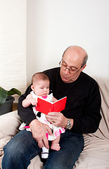 Image showing Grandpa reading red book to baby girl