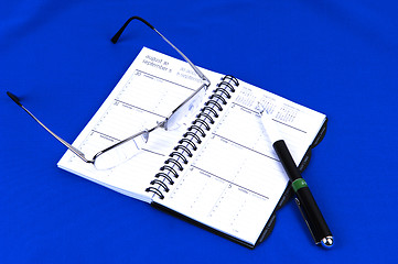 Image showing A day timer with glasses on blue.