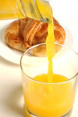 Image showing Pouring orange juice with croissant