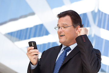 Image showing Businessman Looking at Cell Phone Clinches His Fist in Joy