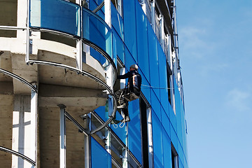 Image showing Builder fixing glass on tall building