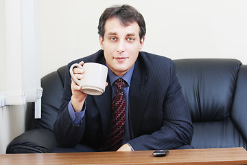 Image showing Businessman with cup sitting on sofa