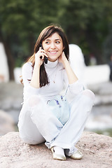 Image showing Woman sitting on stone with cellphone
