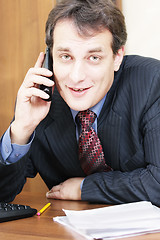 Image showing Smiling businessman at desk with phone