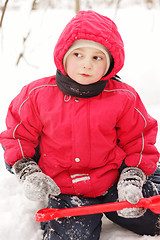 Image showing Little kid in red jacket sitting with shovel