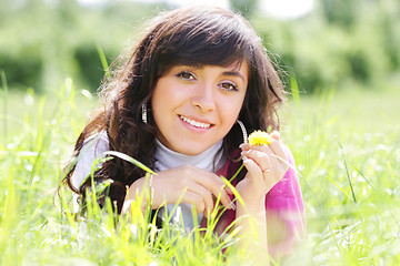 Image showing Smiling brunette in grass with dandelion