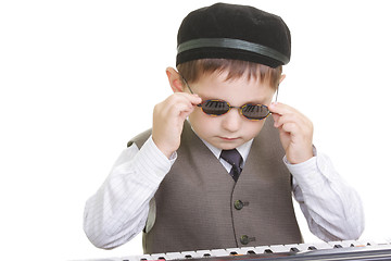 Image showing Cute kid adjusting spectacles at piano keyboard