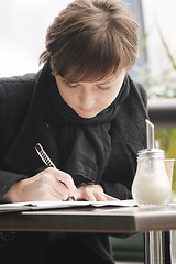 Image showing Woman in black coat writing