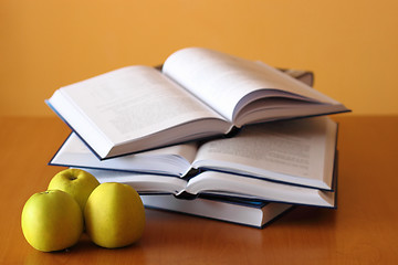 Image showing three green apples and four opened books on the desk