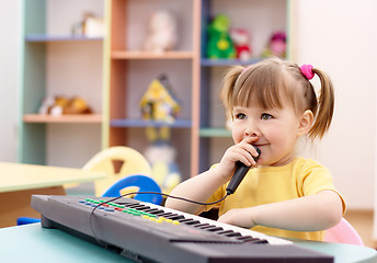 Image showing Girl play on a piano and sing in microphone