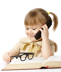 Image showing Cute little girl with book talking to a cell phone