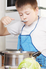 Image showing Boy testing soup from pan