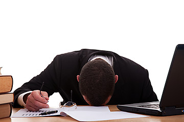 Image showing Stressed young man sitting at a table among books and laptop