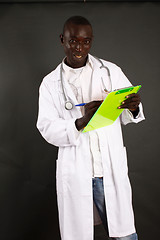 Image showing Doctor writing on a clipboard standing isolated over a black background
