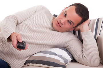 Image showing casual man, lying on the couch, watching television with the command at hand