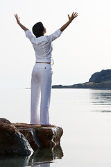 Image showing Young woman meets sunrise staying barefoot on the sea stone