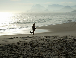 Image showing Woman walking with her dog on the beach sand