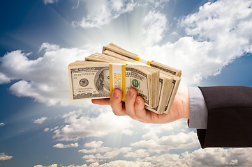 Image showing Male Hand Holding Stack of Cash Over Clouds and Sky