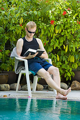 Image showing young man reading nearby the swimming pool